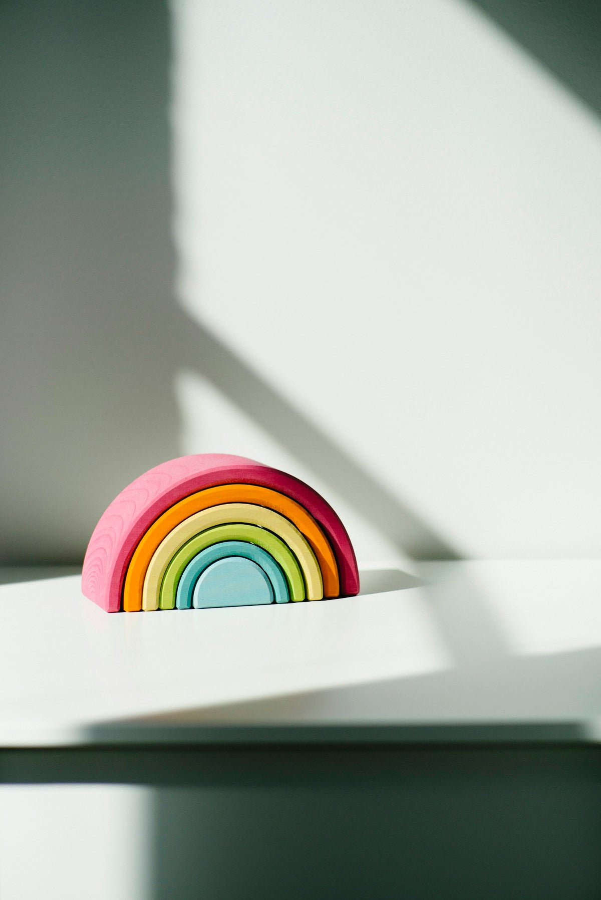 Juguete apilable de madera en forma de arcoiris, tonos pastel, luz suave